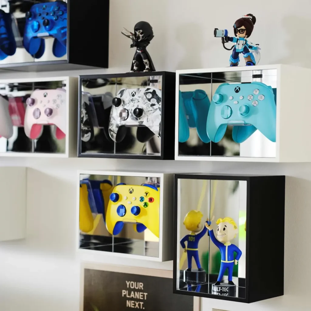 คอนโทรลเลอร์ Xbox หลายสีจัดแสดงอยู่ในกล่องหรือตู้สีขาวและสีดำ พร้อมของสะสมรูปตัวละคร